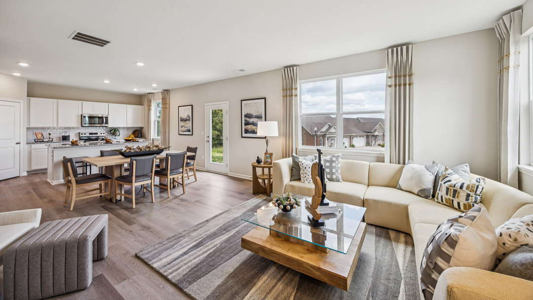 Living room with double window overlooking the backyard, L shaped couch, nightstand, coffee table, and accent chair.