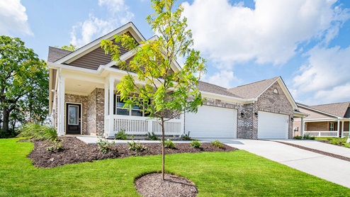 Low maintenance paired villa front exterior with tree line in back of home