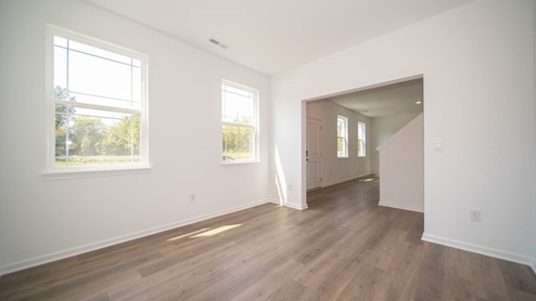 Den adjacent to entryway with two windows and wood laminate flooring.