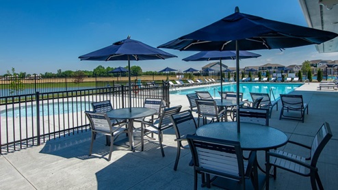 Gated outdoor pool with umbrella covered tables and pool chase chairs.