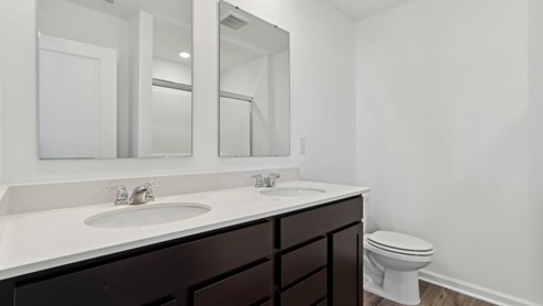 Primary bathroom with dual vanity, white quartz counter top, brown cabinetry, and laminate flooring.