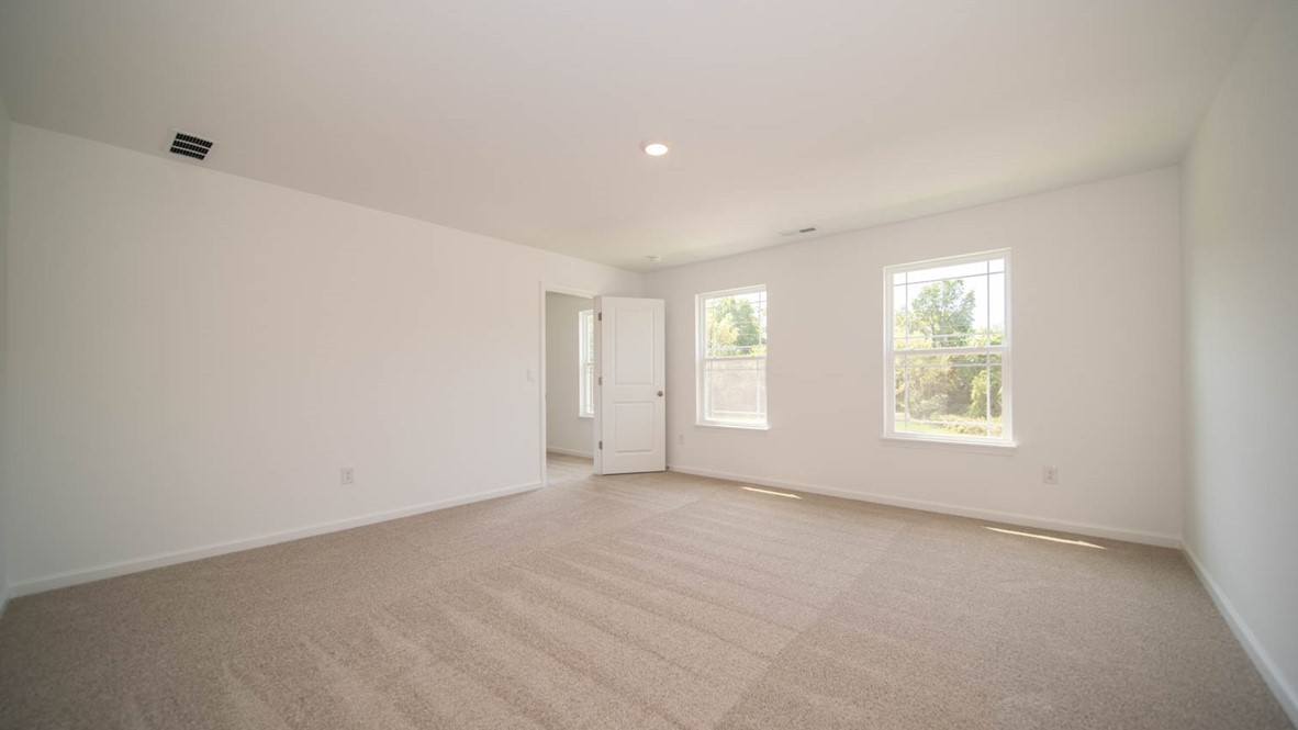 Primary bedroom with two windows and carpet flooring.