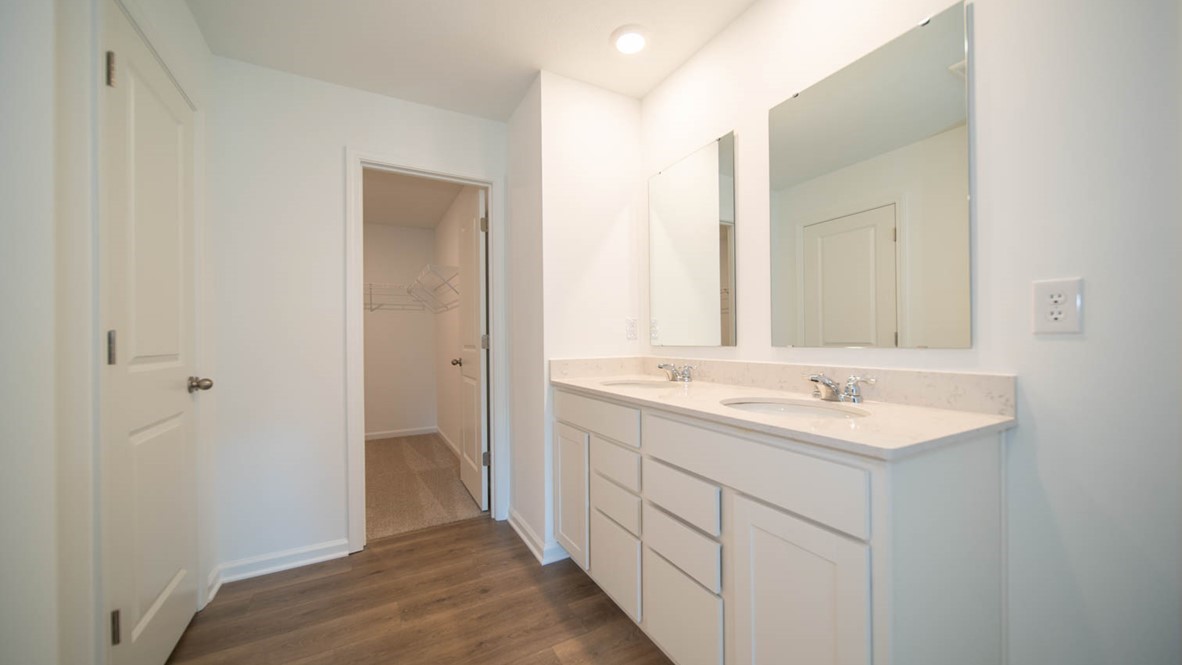 Primary bathroom with a double-sink vanity, vinyl flooring and a walk-in closet.