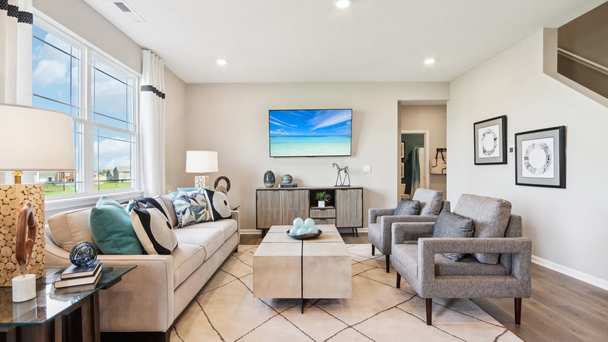 Spacious living room with brown flooring, white walls and windows