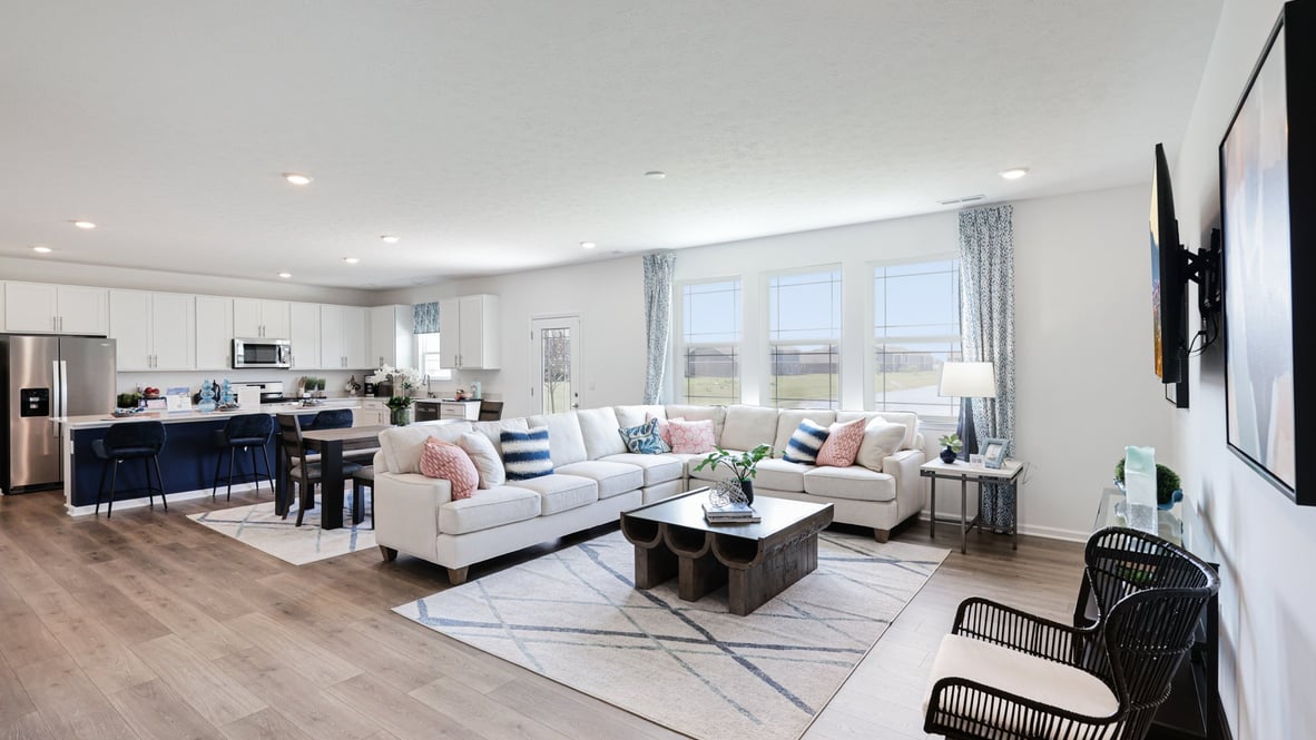 Spacious living room with brown flooring, white walls and windows