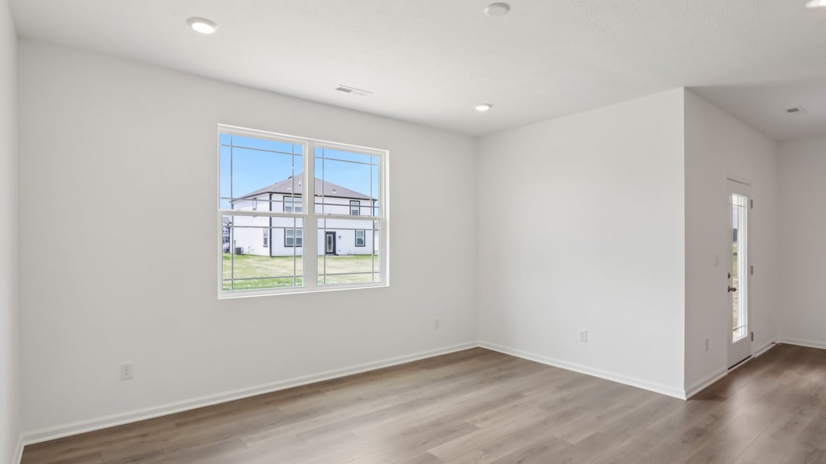 Spacious living room with brown flooring, white walls and windows