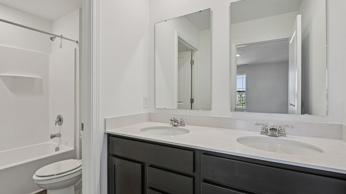 hall bathroom with two sinks, dark cabinets, private commode and tub shower