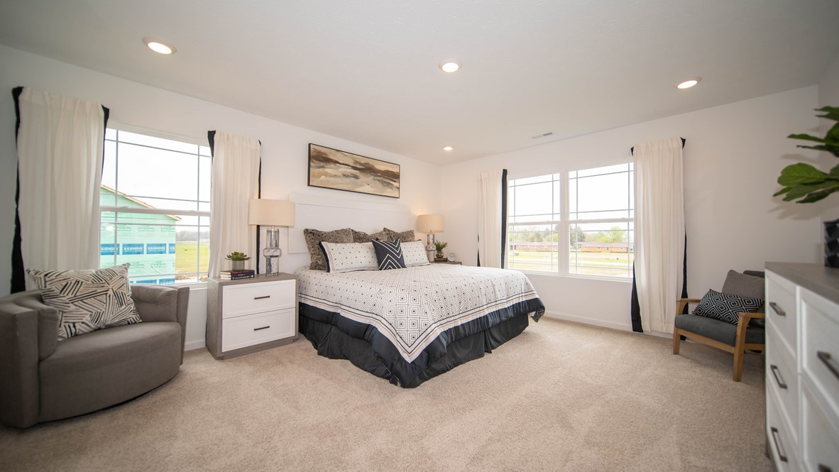 primary bedroom with king bed dresser chair and multiple windows