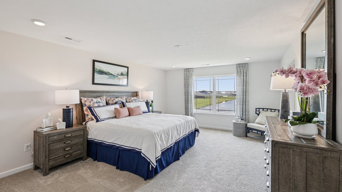 Spacious primary bedroom with beige carpet, white walls and two windows