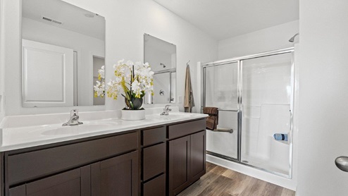 Colonial Heights Bellamy model home bathroom with dual vanity sinks and walk in shower with LVP flooring