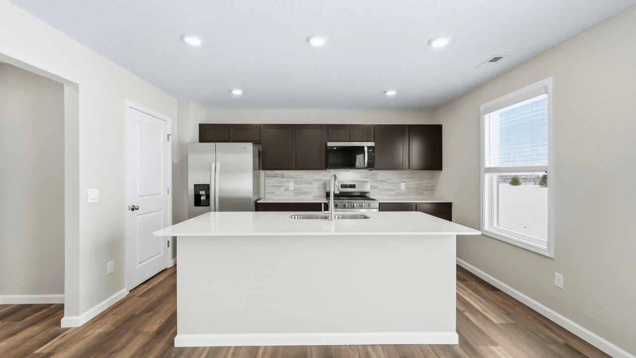 kitchen with sarsaparilla cabinets, quartz counters, stainless steel appliances, tile backsplash, and center island with dishwasher, sink, and bar seating.