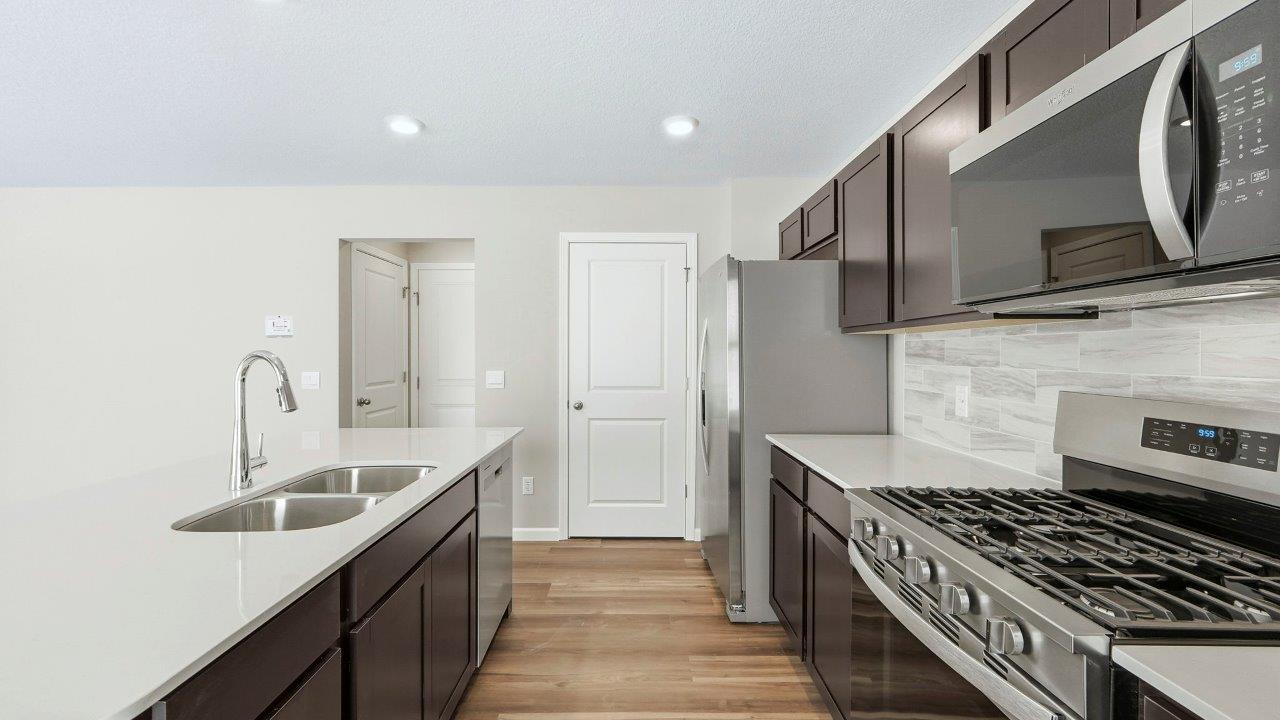 kitchen with sarsaparilla cabinets, quartz counters, stainless steel appliances, tile backsplash, and center island with dishwasher, sink, and bar seating.