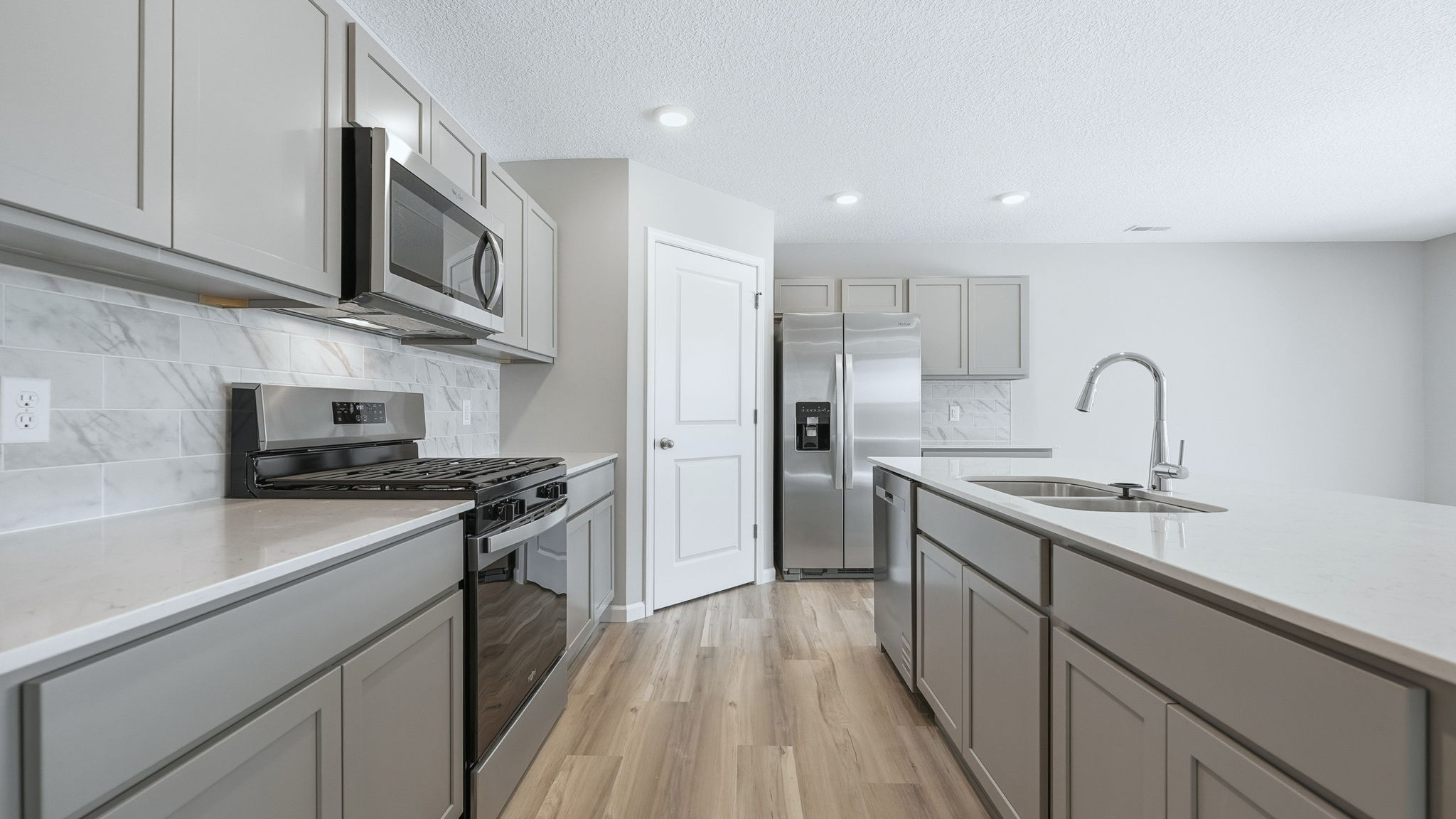 Trader's Trace Chatham kitchen with grey cabinets, quartz counters, stainless steel appliances, corner pantry, backsplash, and center island with bar seating