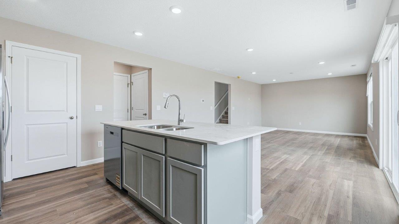 kitchen island with grey cabinets, quartz counter, sink, stainless steel dishwasher, and bar seating.