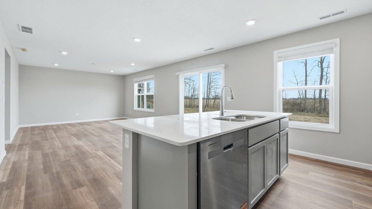 kitchen island with grey cabinets, quartz counter, sink, stainless steel dishwasher, and bar seating.