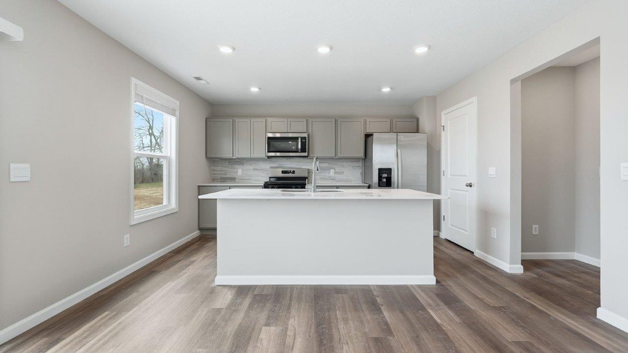 kitchen with grey shaker cabinets, quartz counters, full stainless steel appliance set, ceramic tile backsplash, and mohawk eastmont lvp flooring