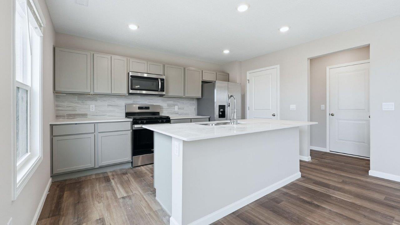 kitchen with grey shaker cabinets, quartz counters, full stainless steel appliance set, ceramic tile backsplash, and mohawk eastmont lvp flooring