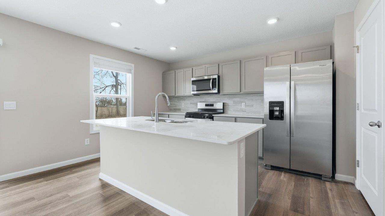 kitchen with grey shaker cabinets, quartz counters, full stainless steel appliance set, ceramic tile backsplash, and mohawk eastmont lvp flooring
