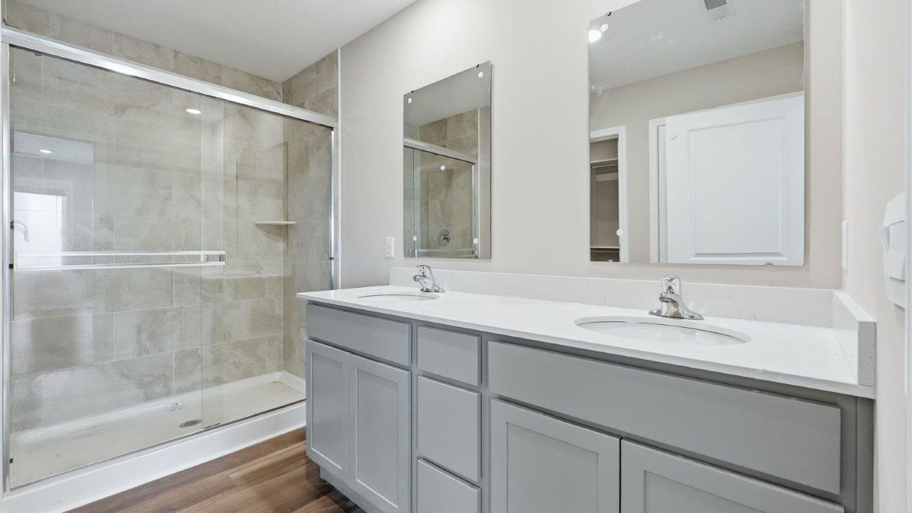 primary ensuite bathroom with dual sinks, walk-in tile shower, quartz counters, and grey cabinets