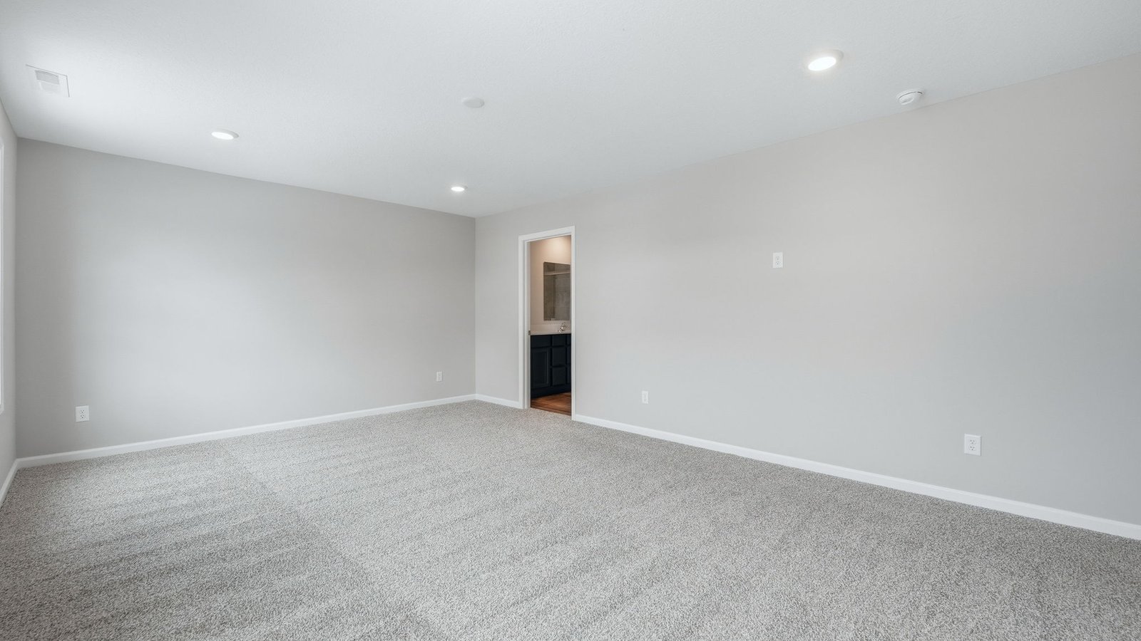 primary bedroom with biege carpet, popular grey walls, 2 windows, and ensuite bathroom and walk-in closet