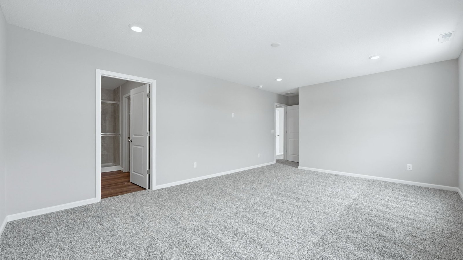 primary bedroom with biege carpet, popular grey walls, 2 windows, and ensuite bathroom and walk-in closet