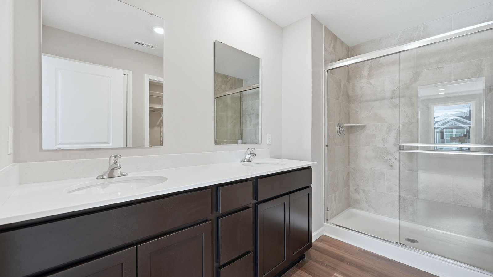 primary ensuite bathroom with dual sinks, walk-in ceramic tile shower, and lvp flooring