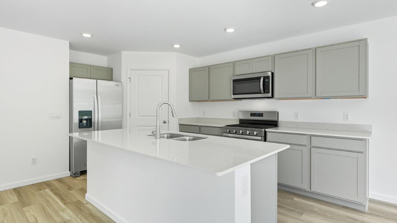 parlor bluffs cabral kitchen with large island, grey cabinets, quartz counters, corner pantry, and stainless steel appliances