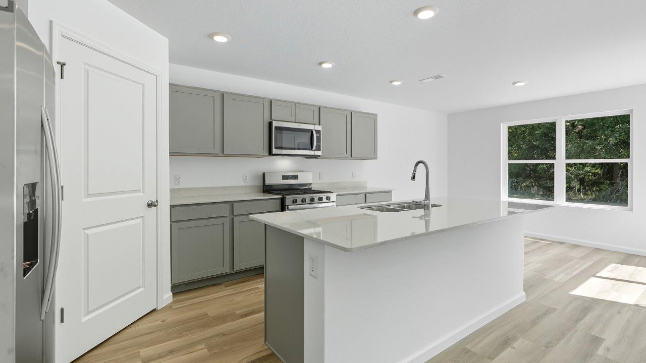 parlor bluffs cabral kitchen with large island, grey cabinets, quartz counters, corner pantry, and stainless steel appliances