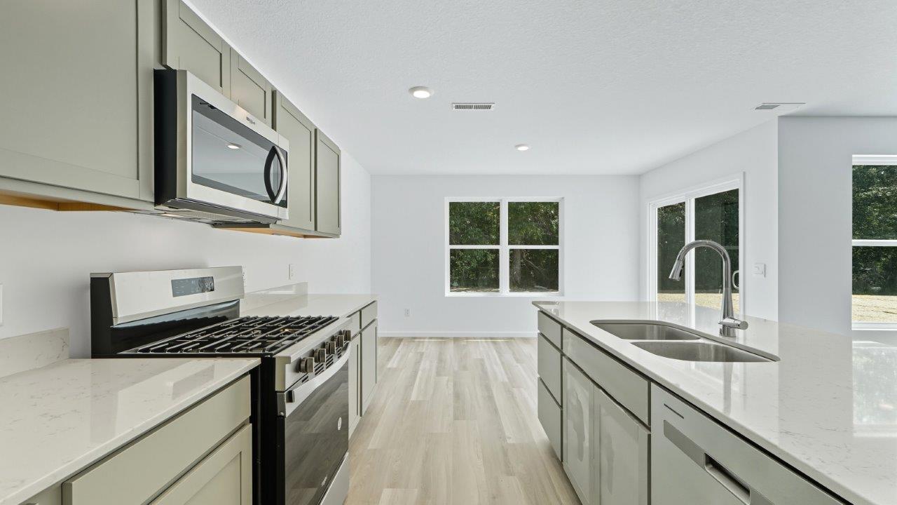 parlor bluffs cabral kitchen with large island, grey cabinets, quartz counters, corner pantry, and stainless steel appliances