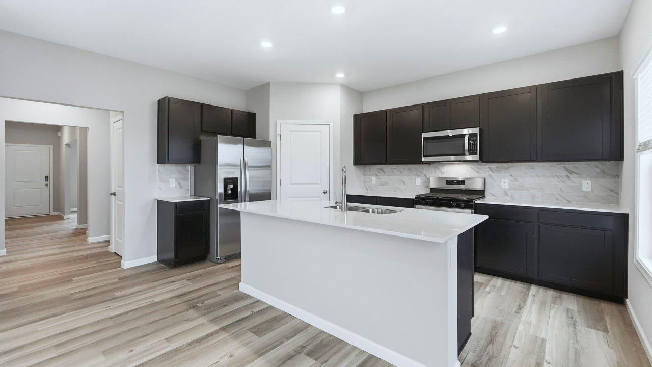 open layout kitchen with center island, sarsaparilla cabinets, quartz counters, stainless steel appliances, corner pantry