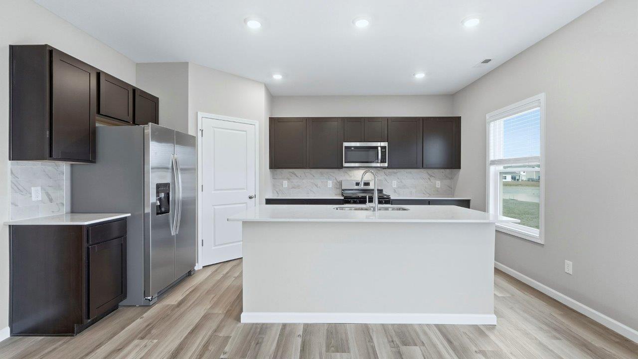 open layout kitchen with center island, sarsaparilla cabinets, quartz counters, stainless steel appliances, corner pantry