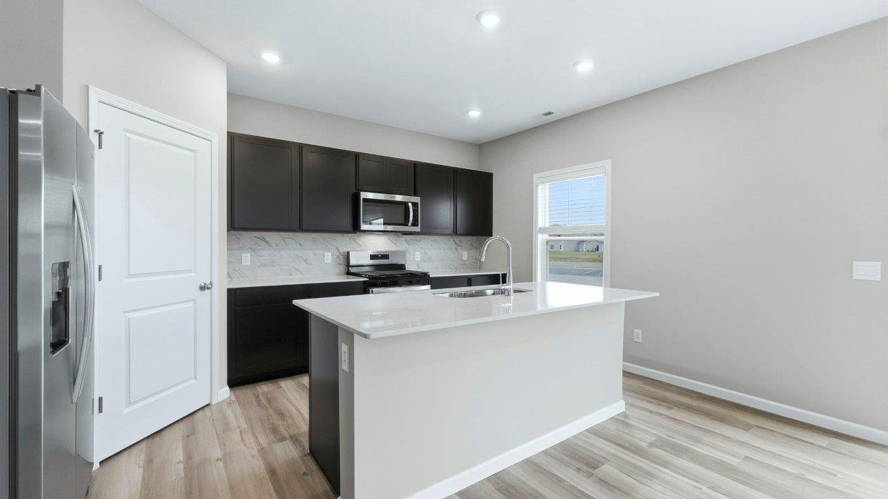 open layout kitchen with center island, sarsaparilla cabinets, quartz counters, stainless steel appliances, corner pantry
