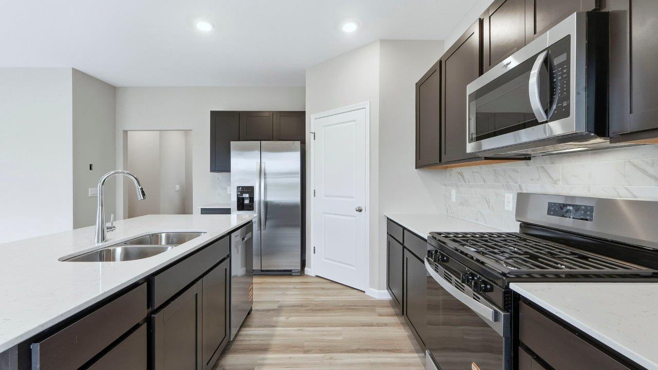 open layout kitchen with center island, sarsaparilla cabinets, quartz counters, stainless steel appliances, corner pantry