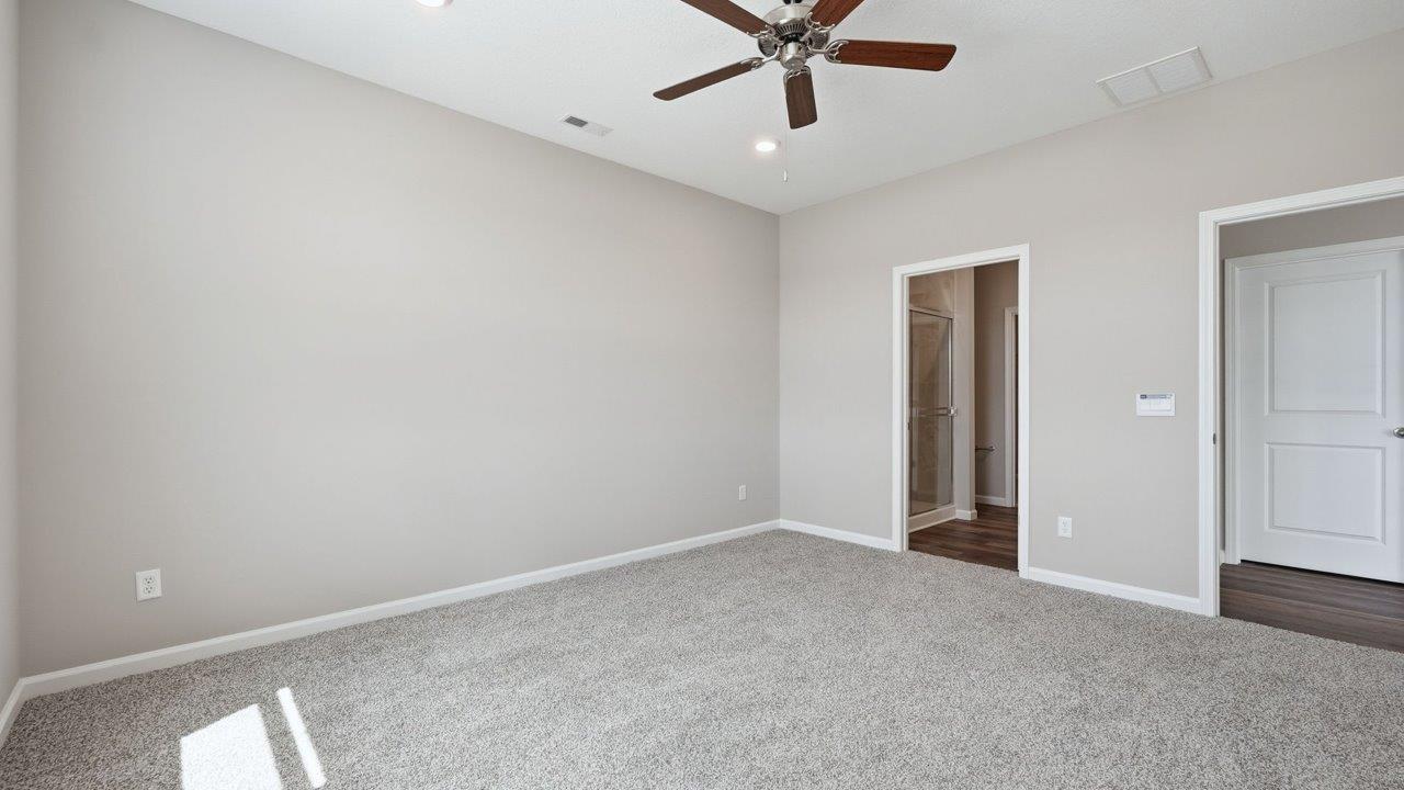 estates at signal ridge harmony villa primary bedroom with 2 windows, carpet, ceiling fan, and ensuite bathroom and closet