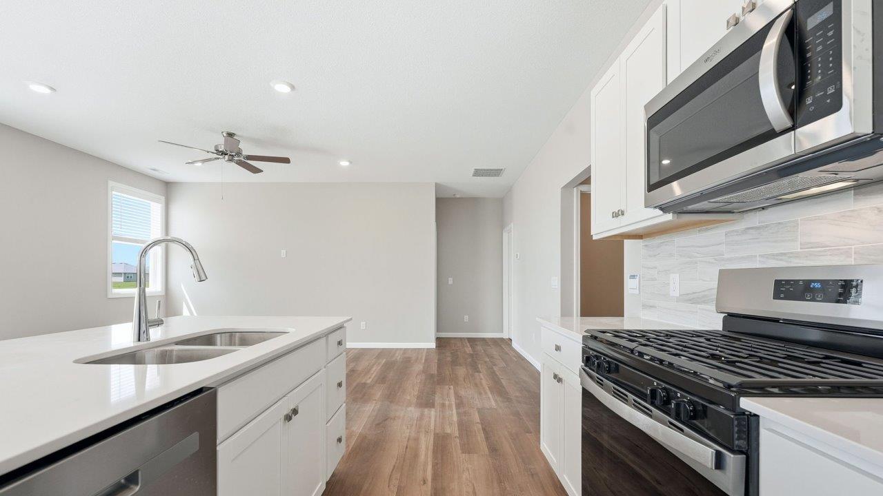 estates at signal ridge harmony villa kitchen with white cabinetry, stainless steel appliances, ceramic tile backsplash, corner pantry, and center island with bar seating