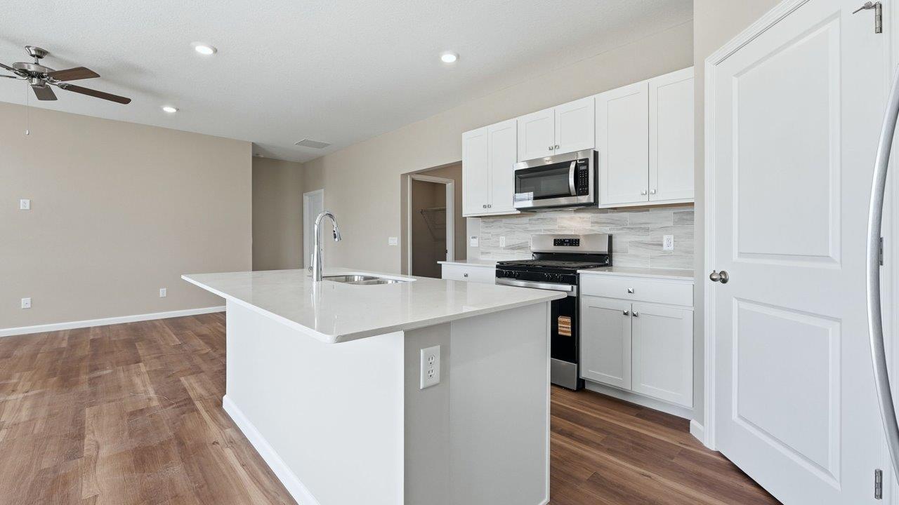 estates at signal ridge harmony villa kitchen with white cabinetry, stainless steel appliances, ceramic tile backsplash, corner pantry, and center island with bar seating