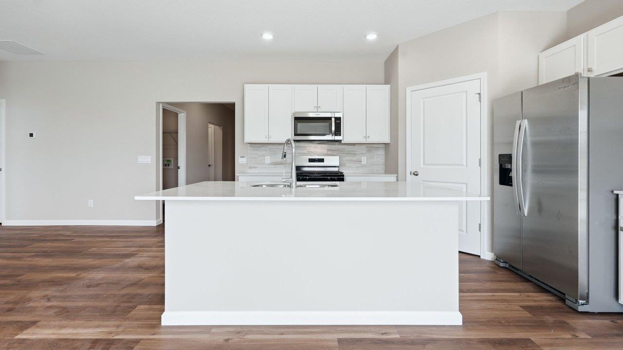 estates at signal ridge harmony villa kitchen with white cabinetry, stainless steel appliances, ceramic tile backsplash, corner pantry, and center island with bar seating