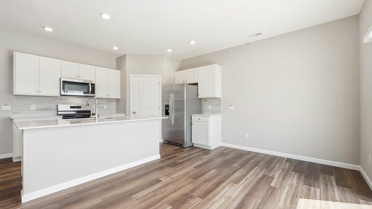 estates at signal ridge harmony villa kitchen with white cabinetry, stainless steel appliances, ceramic tile backsplash, corner pantry, and center island with bar seating