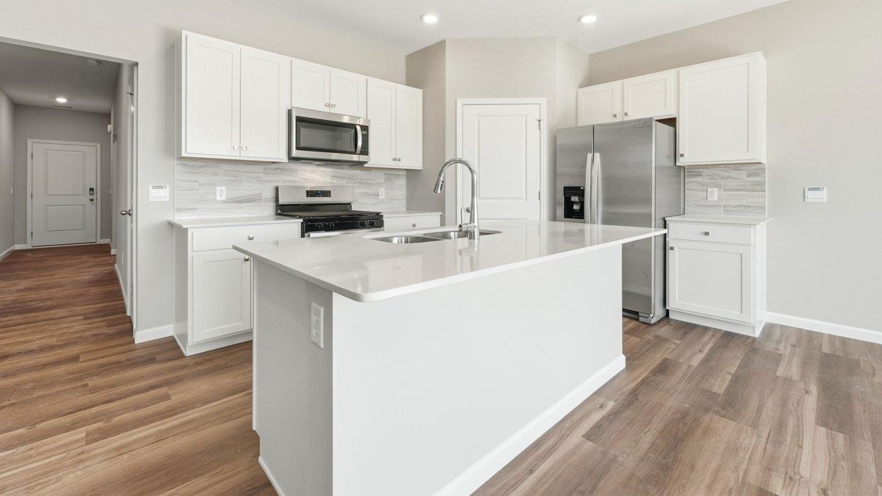 estates at signal ridge harmony villa kitchen with white cabinetry, stainless steel appliances, ceramic tile backsplash, corner pantry, and center island with bar seating