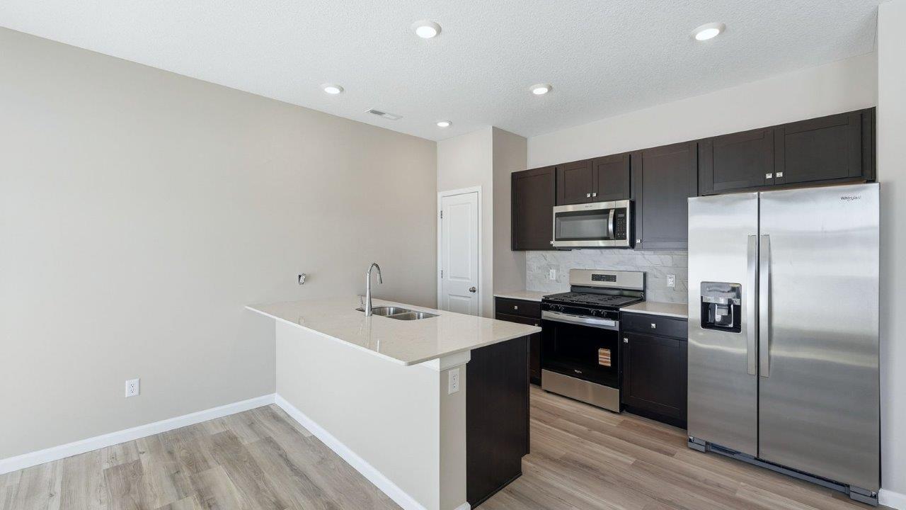 kitchen with sarsaparilla shaker cabinets, quartz counters, stainless steel appliances, ceramic tile backsplash, and island with seating