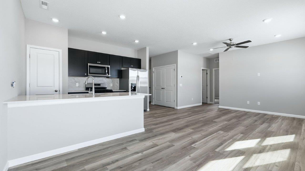 kitchen with sarsaparilla shaker cabinets, quartz counters, stainless steel appliances, ceramic tile backsplash, and island with seating