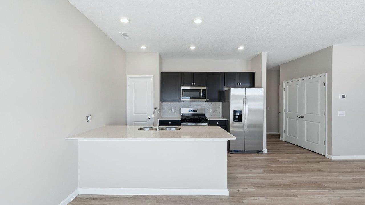 kitchen with sarsaparilla shaker cabinets, quartz counters, stainless steel appliances, ceramic tile backsplash, and island with seating