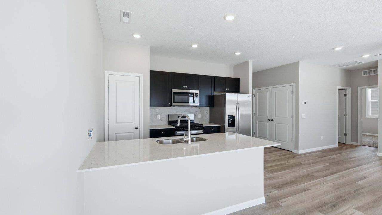 kitchen with sarsaparilla shaker cabinets, quartz counters, stainless steel appliances, ceramic tile backsplash, and island with seating