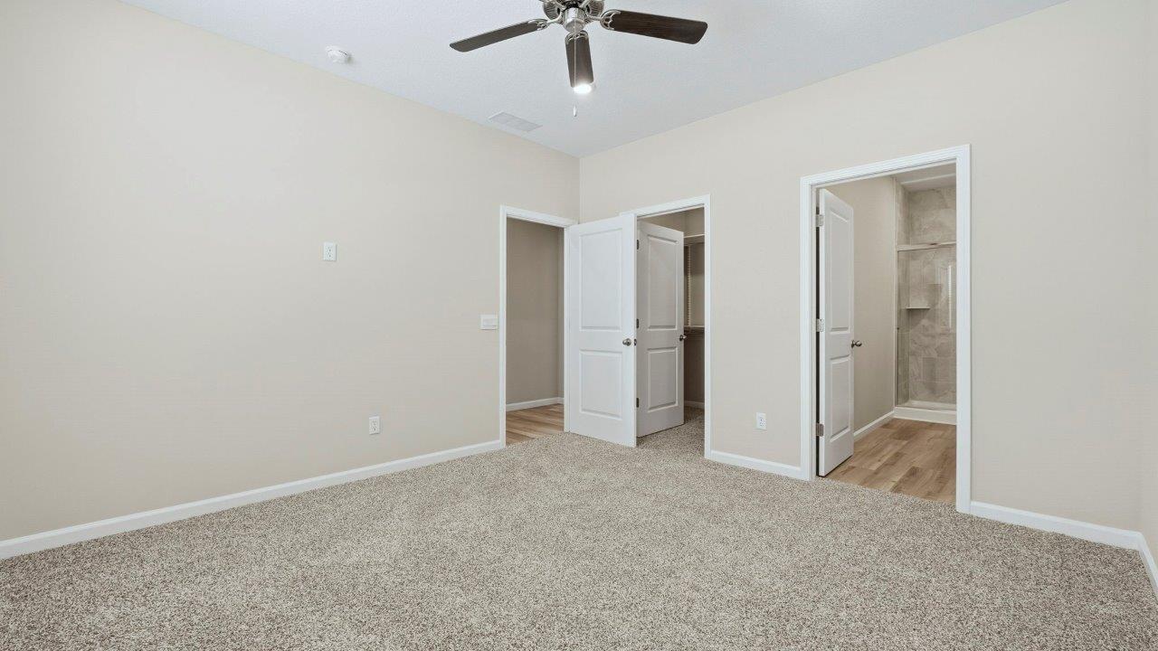 primary bedroom with carpet, fan, and ensuite bath and closet