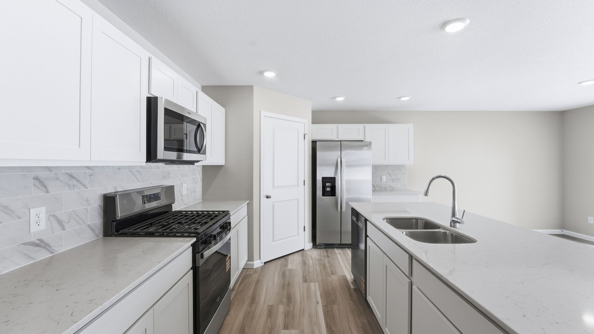 kitchen with white cabinets, tile backsplash, quartz counters, appliances, center island with bar seating, and corner pantry