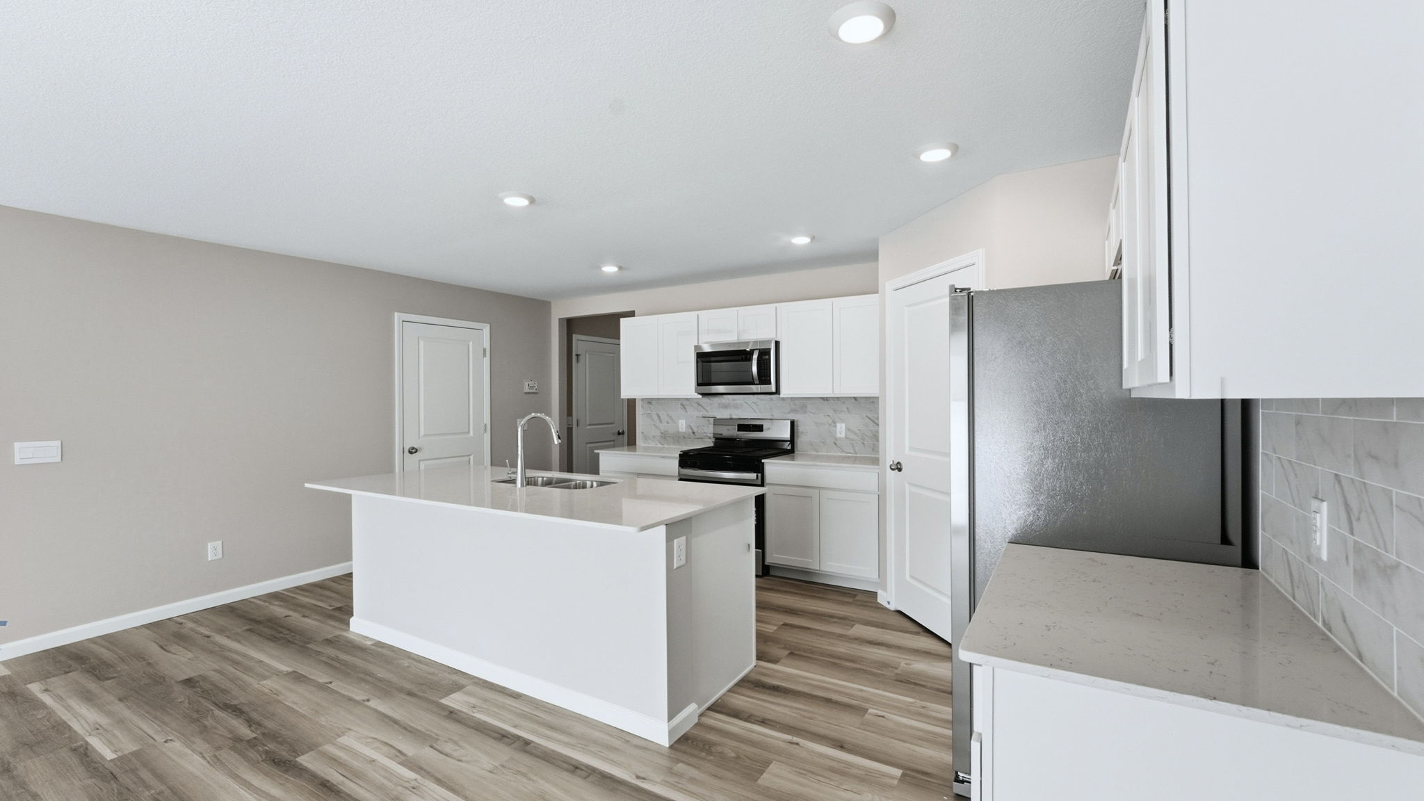 kitchen with white cabinets, tile backsplash, quartz counters, appliances, center island with bar seating, and corner pantry