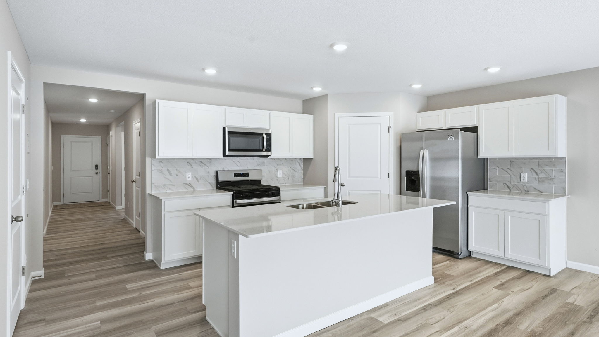 kitchen with white cabinets, tile backsplash, quartz counters, appliances, center island with bar seating, and corner pantry