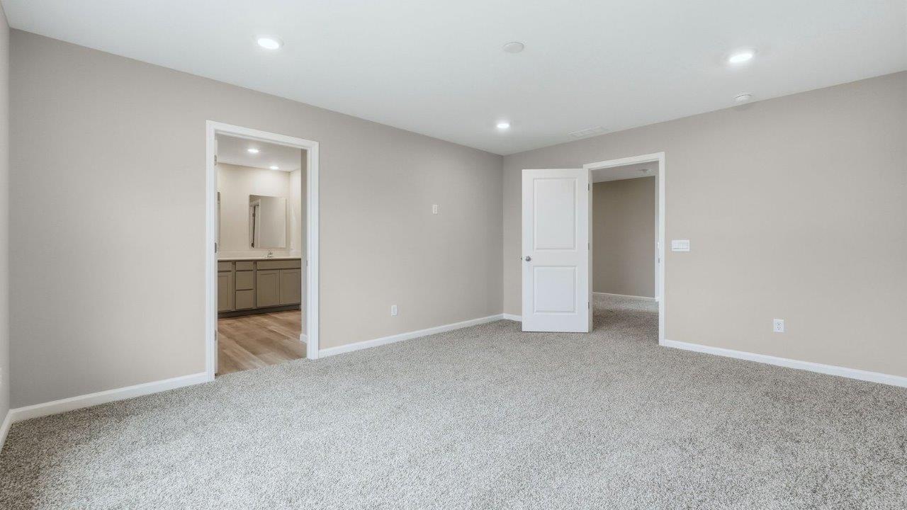 spacious primary bedroom with beige carpet, popular grey walls, and ensuite bath and walk-in closet