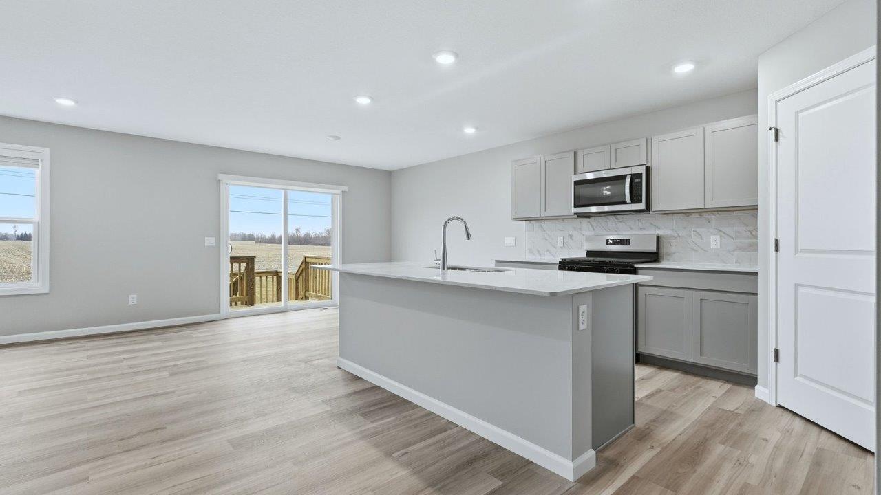 kitchen with grey cabinets, stainless steel appliances, corner pantry, ceramic tile backsplash, and quartz countertops