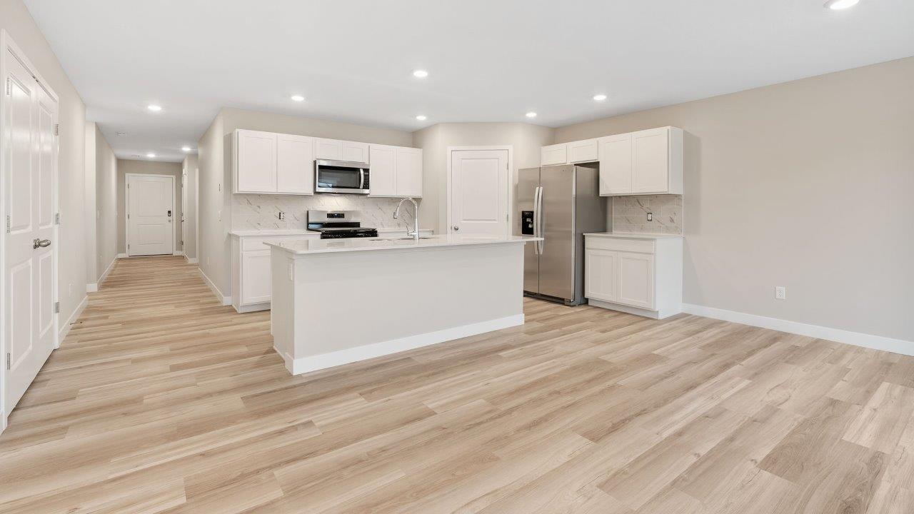 fawn creek estates freeport - kitchen with white cabinets, quartz countertops, tile backsplash, corner pantry, stainless steel appliances, lvp flooring, and island with seating